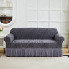 A charcoal gray jacquard sofa cover with a wavy pattern and an elastic skirt displayed on a white couch.