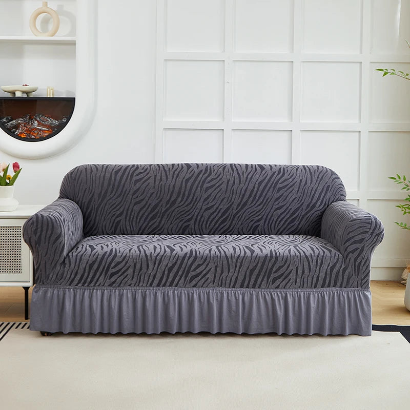 A charcoal gray jacquard sofa cover with a wavy pattern and an elastic skirt displayed on a white couch.