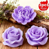 Three silicone molds shaped like purple roses and peonies resting on a wooden surface.