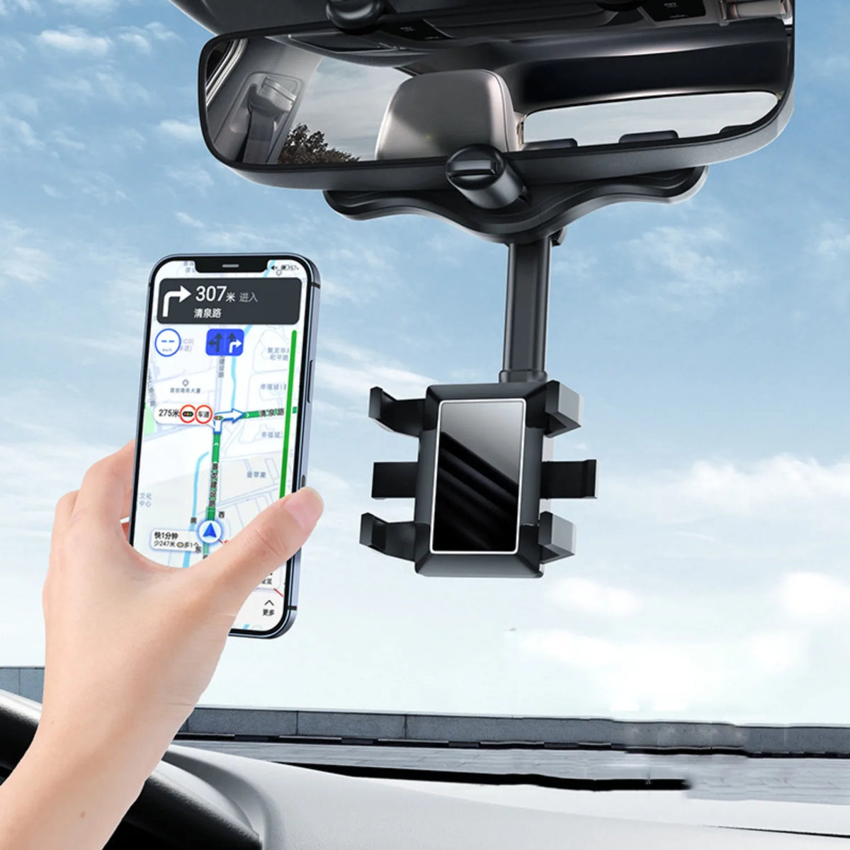 A hand holds a smartphone attached to a universal rearview mirror phone mount with a rotatable arm installed on a vehicle's i