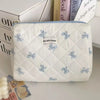 A white quilted cosmetic bag with light blue bow print and a light blue trim, resting on a white surface.