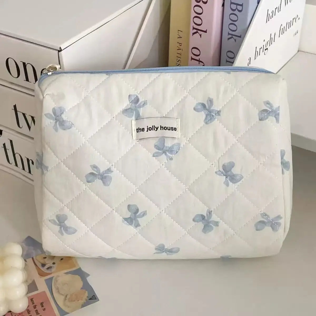 A white quilted cosmetic bag with light blue bow print and a light blue trim, resting on a white surface.