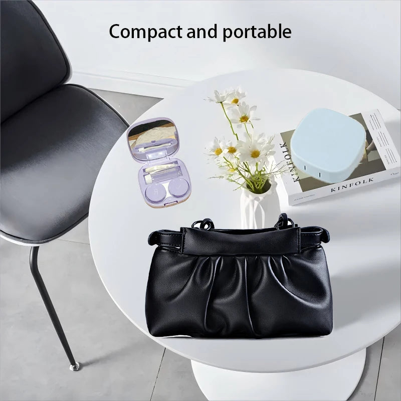 A black compact contact lens travel case is displayed on a white table next to a chair.
