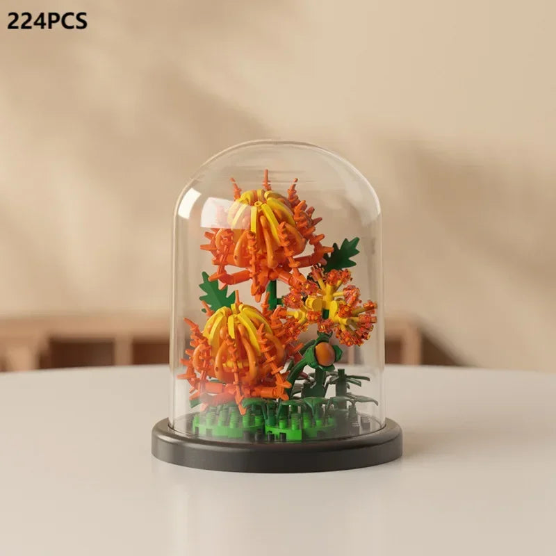 A clear glass display shows an orange and yellow eternal rose bouquet made of micro building blocks.