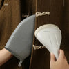 A hand holds a white portable ironing board glove against a brown coat.