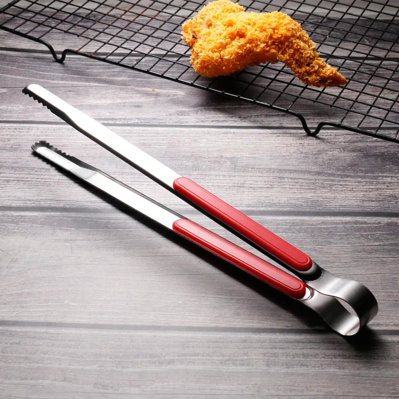 A pair of shiny stainless steel BBQ tongs with red handles resting on a dark wire grill grate.