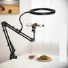 A black adjustable phone stand with an overhead light illuminates a plate of food on a white table.