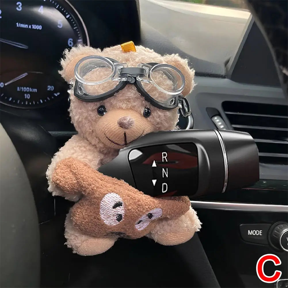 A cute plush bear is placed on a car gear shift cover in a vehicle interior.