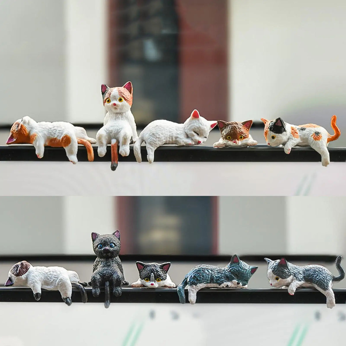 A collection of ten small cat figurines in various orange, white, and gray colors arranged horizontally.