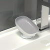 A white, leaf-shaped suction cup soap dish is placed on a white bathroom sink.