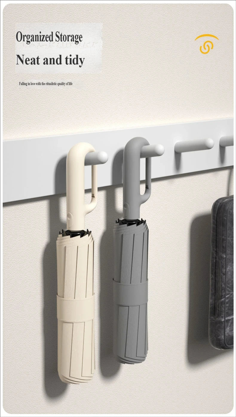 Two automatic folding umbrellas, one cream and one gray, are displayed hanging on a wall.