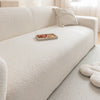 A white plush sofa cover with a light beige throw pillow and a wooden tray of snacks on the seat.