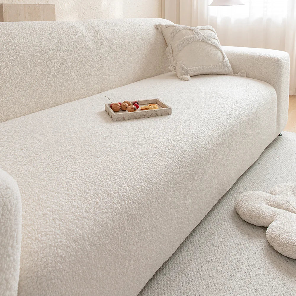 A white plush sofa cover with a light beige throw pillow and a wooden tray of snacks on the seat.