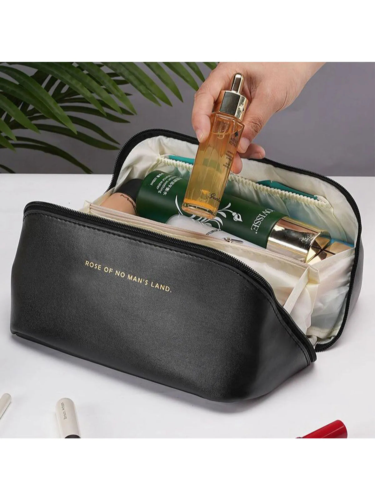 A hand is opening a black leather travel makeup organizer bag revealing a gold perfume bottle inside.