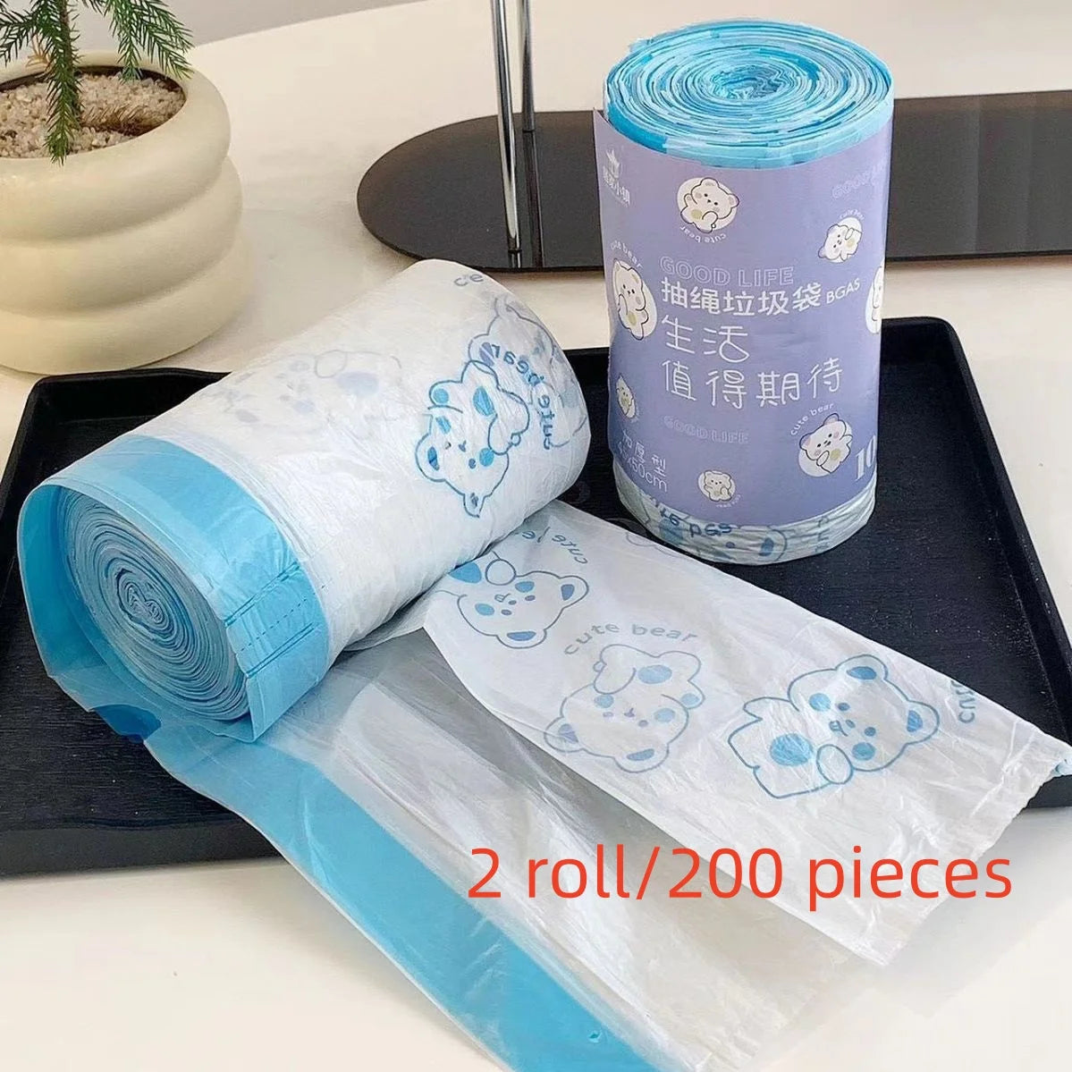 A roll of clear drawstring trash bags with blue accents is shown next to a potted plant.