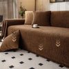 A brown chenille sofa throw with tassel edges is draped over a sofa, featuring geometric embroidery on the fabric.