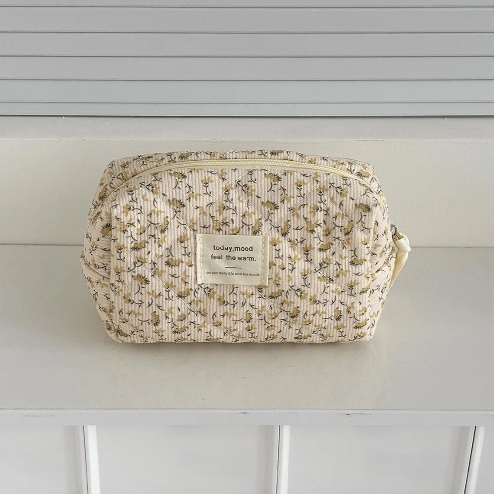 A beige floral quilted cosmetic bag resting on a white surface.