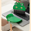 A hand is using a green cartoon broom and dustpan set to clean a laptop or desk surface.
