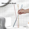 A hand holds a set of two silicone straw cleaning brushes, one pink and one light blue, against a white tiled background.