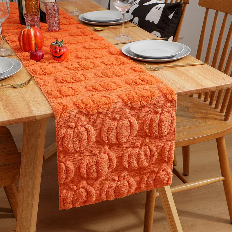 Orange knitted table runner with pumpkin patterns set on a wooden table for seasonal dining.