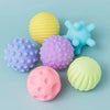 A collection of six soft, textured sensory balls in various pastel colors including yellow, blue, purple, and pink.