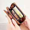 A hand holds a brown vintage RFID blocking short wallet with a zipper closure, showing several cards inside.