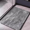 A gray marble-look non-slip bathroom mat is placed on a light-colored floor next to a shower area.