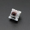 A close-up view of a white mechanical keyboard switch housing with a brown plastic stem.
