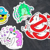 A collection of colorful die-cut vinyl stickers featuring various designs and text on a black chalkboard background.