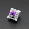 A close-up view of a clear plastic mechanical keyboard switch with a purple housing and gold pins.