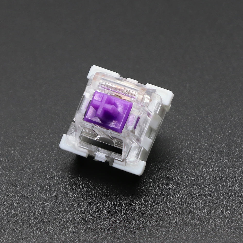 A close-up view of a clear plastic mechanical keyboard switch with a purple housing and gold pins.