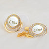 Gold-toned rhinestone pacifier featuring the name Lina on a white disc with a clip.
