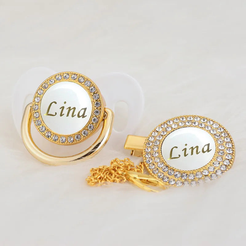 Gold-toned rhinestone pacifier featuring the name Lina on a white disc with a clip.