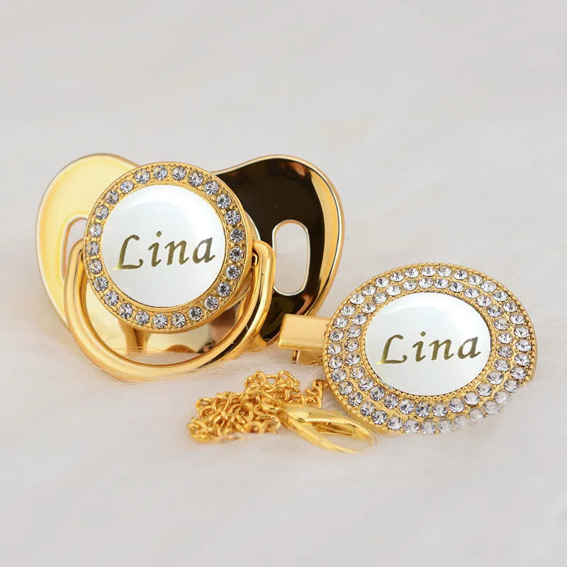 Gold rhinestone pacifier featuring the name Lina on a white disc and clip.