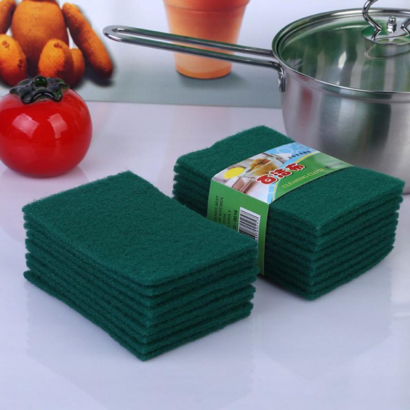 A stack of green microfiber kitchen scrubbing sponges next to a cooking pot and a red tomato.