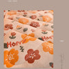 A close-up of a peach-colored fabric quilt featuring floral embroidery and text on a neutral background.