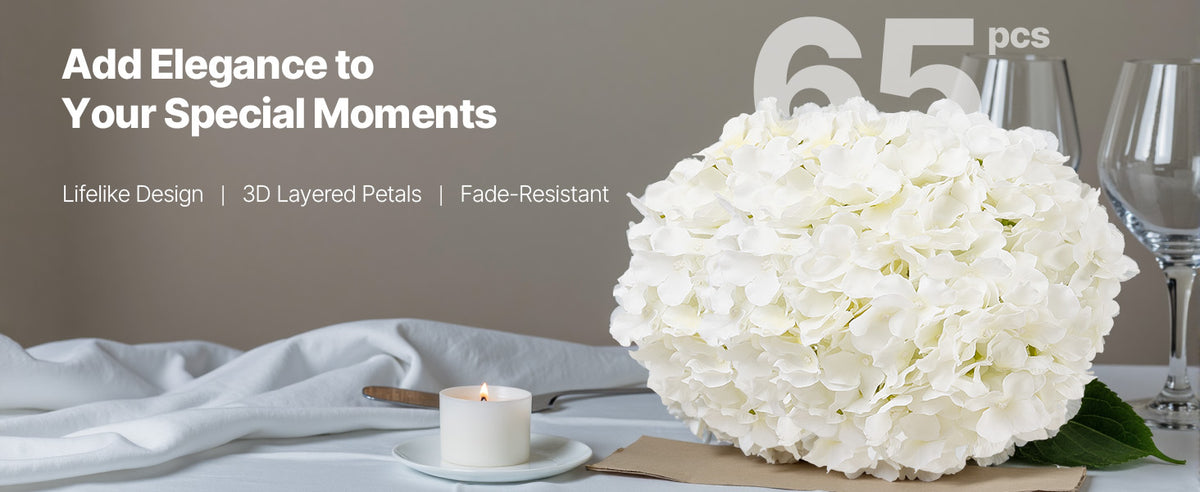 A large bouquet of white hydrangeas is displayed on a table with a candle and glassware.