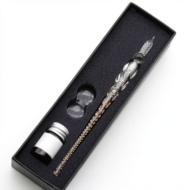 Pluma de inmersión de cristal con juego de tinta dorada, exhibida dentro de una caja negra.
