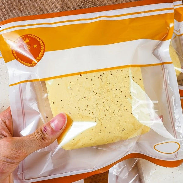 A hand holds a yellow slow-rising toast squishy stress relief toy packaged in an orange and white plastic bag.