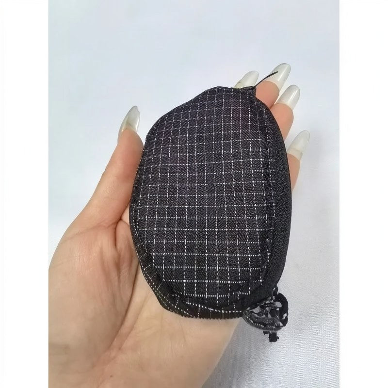Une main tient un écouteur en nylon à carreaux noirs et une pochette de clés sur un fond blanc.