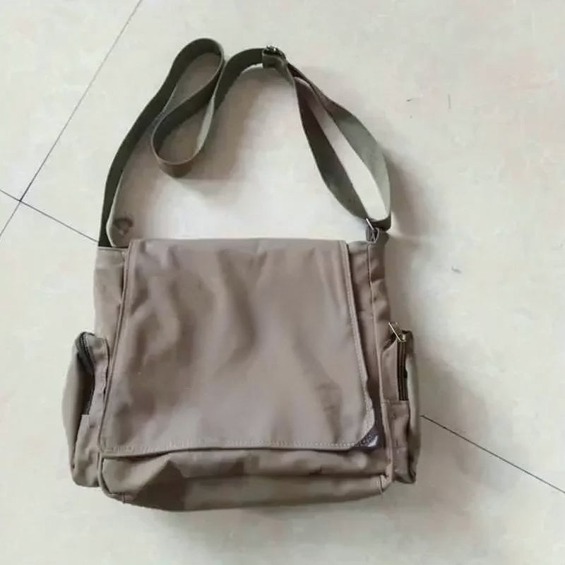 Bolso cruz tipo tote de lona beige con correa oscura y cierre de cremallera sobre una superficie blanca.