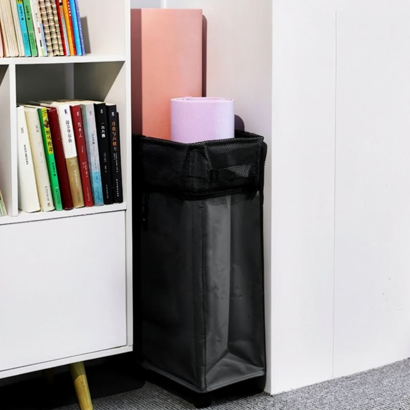 Panier de rangement noir pour linge ou tapis de yoga, posé à côté d'une étagère blanche.