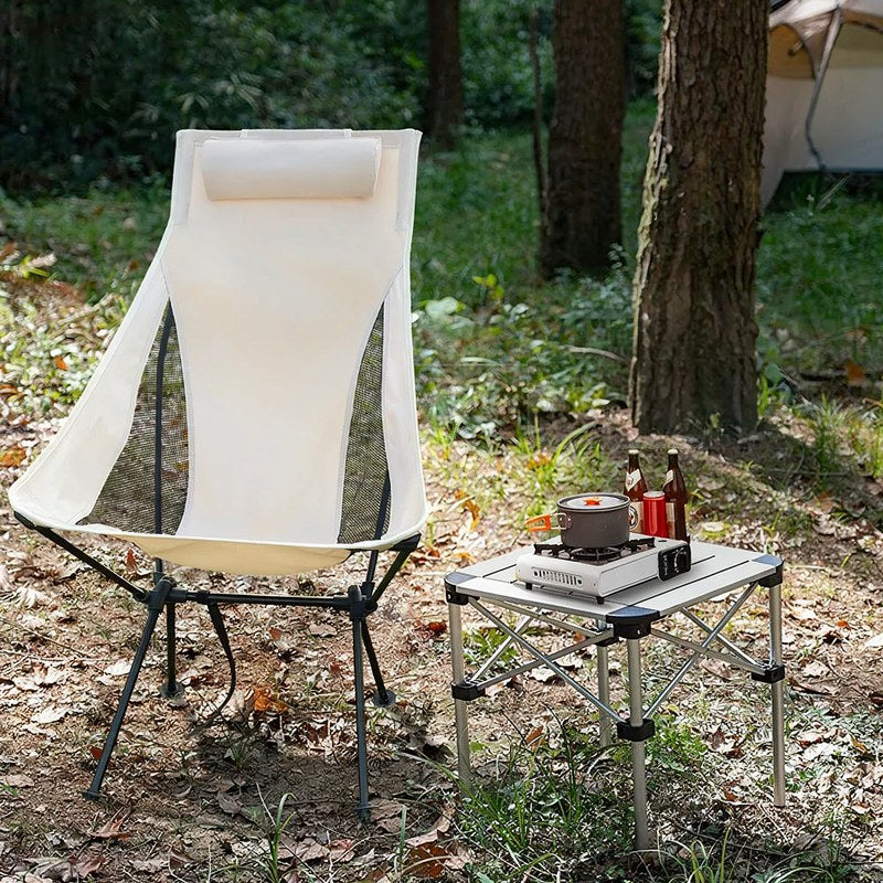 Ein weißer faltbarer Campingstuhl mit Kopfstütze auf einem Holztisch in einer bewaldeten Umgebung.