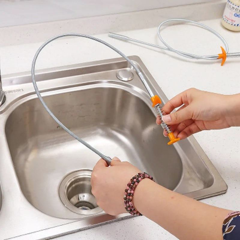 Une main utilise un serpent de nettoyage de siphon avec une pointe à griffe pour nettoyer un évier de cuisine.