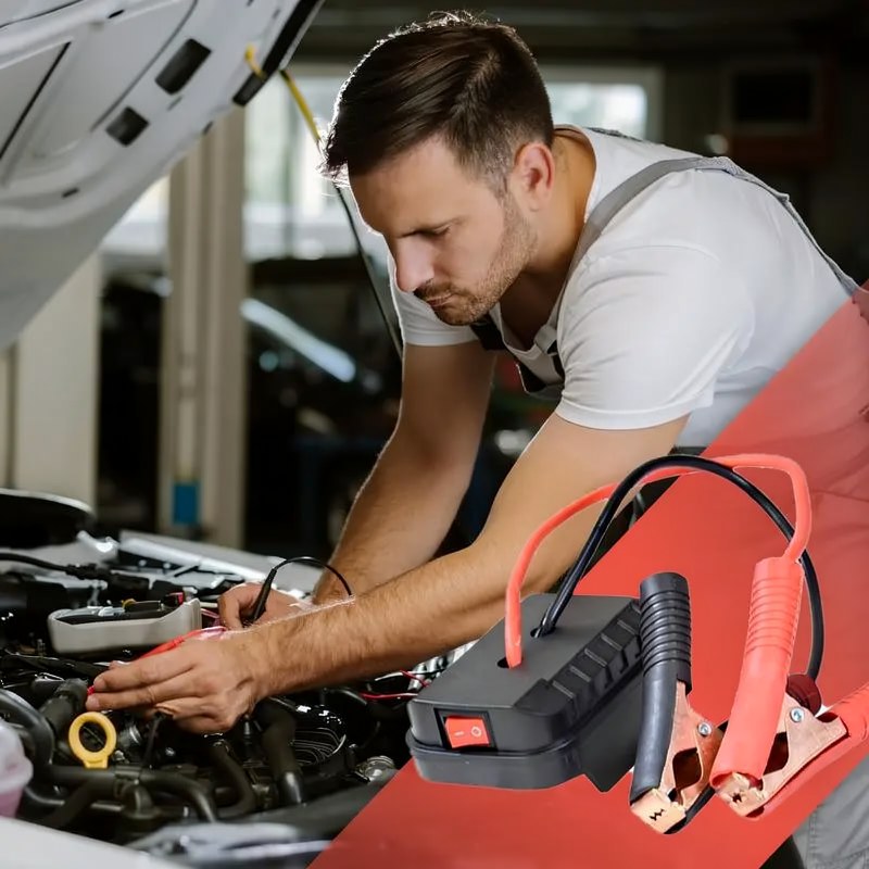 Un homme utilise un démarrage portable sur le moteur d'une voiture dans un garage.