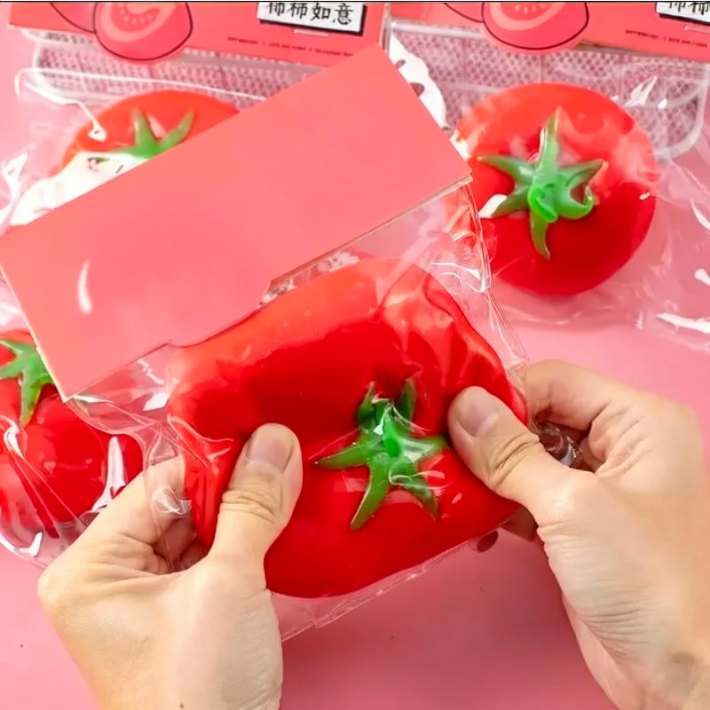 Des mains serrant une balle anti-stress de patate rouge vif dans un emballage transparent.
