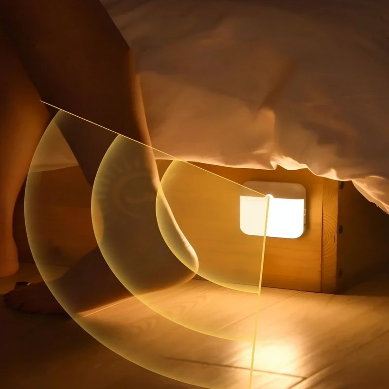 A rechargeable motion sensor night light casts a warm glow on a wooden surface.
