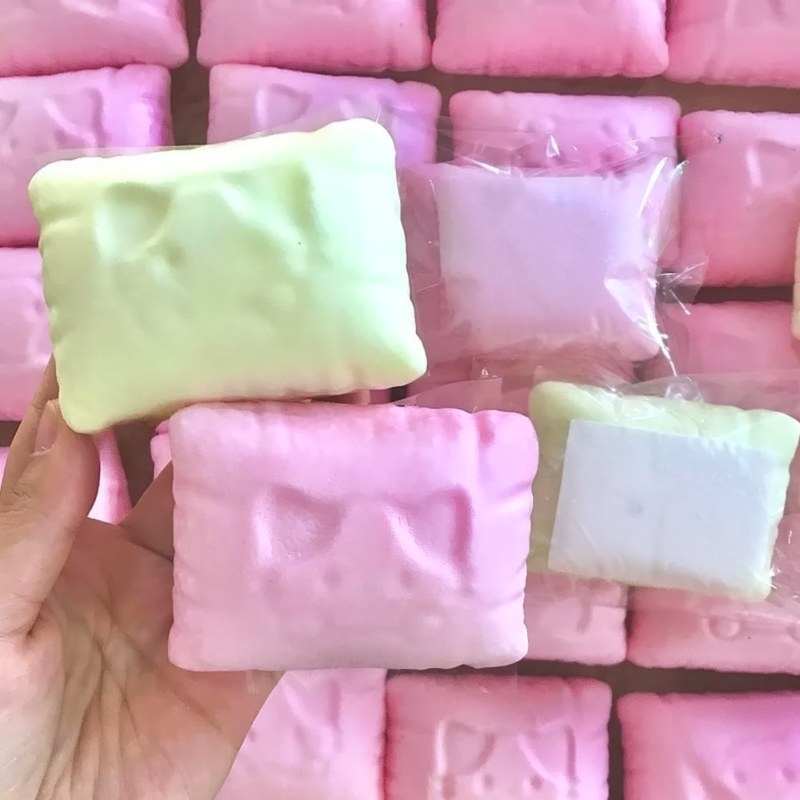 Une main tient un oreiller anti-stress en forme de chat blanc et rose parmi d'autres oreillers similaires.