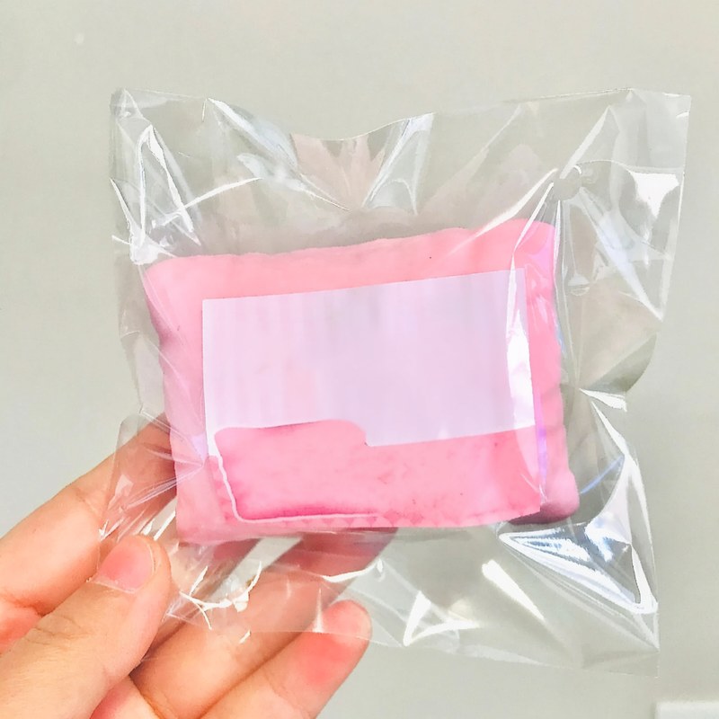 Un oreiller anti-stress rose en forme de chat, dans un sac plastique transparent tenu par une main.