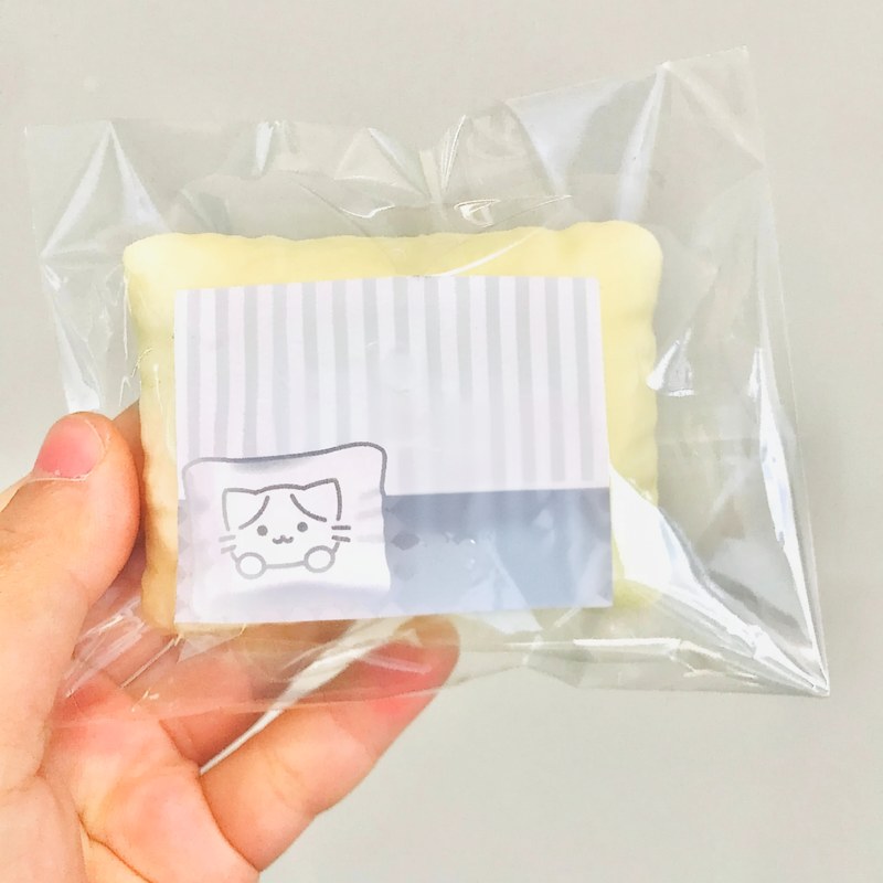 Un oreiller anti-stress en forme de chat, jaune et doux, scellé dans un sac en plastique transparent.